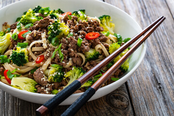 Udon noodles with minced beef and broccoli on wooden table