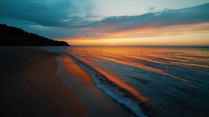 Fototapeta premium Serene beach during sunset with calm waves and a vivid orange and blue sky reflecting on the water surface