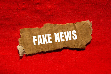 Fake news message written on ripped torn cardbaord paper piece with red background. Conceptual fake...