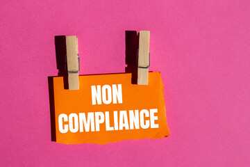 Non compliance message written on ripped torn orange paper piece with pink background. Conceptual...