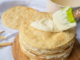 Silicone spatula spreading vanilla custard over a pile of baked thin round buttery layers on a...
