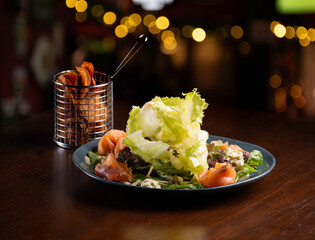 delicious and colorful smoked salmon salad with mixed leaves, cheeses, cold cuts accompanied by sweet potato chips in a restaurant with a blurred background