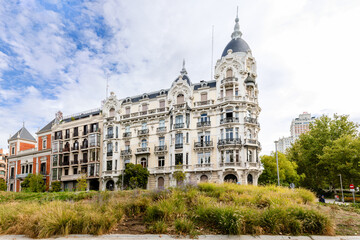 Fototapeta premium Madrid, Spain - october 2, 2024: Details of the different buildings surrounding the Square Spain in Madrid with people walking through its streets in Madrid, Spain
