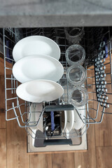 Modern open dishwasher with clean dishes after washing cycle at kitchen