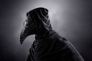 Plague doctor in hooded cloak at night over dark misty background