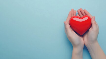 Fototapeta premium Close-Up of Hands Holding Red Heart on Light Blue Background, Top View with Copy Space for Valentine's Day or World Health and Wellness Day Concept