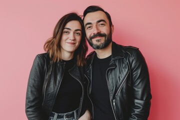 Fototapeta premium Portrait of a content couple in their 30s sporting a classic leather jacket in front of solid color backdrop