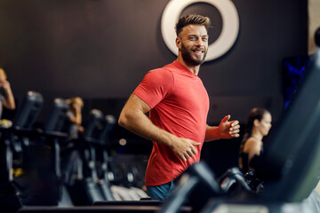 Happy sportsman running on treadmill at gym and smiling at camera.