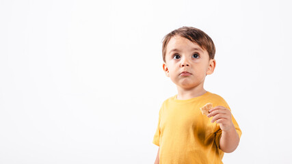 Two-year-old boy with a cookie in his hand looks away with a puzzled face