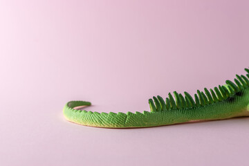 Tail of green lizard toy on pastel pink background. Minimal art concept.