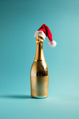 A golden champagne bottle with xmas hat on top on a pastel blue background.