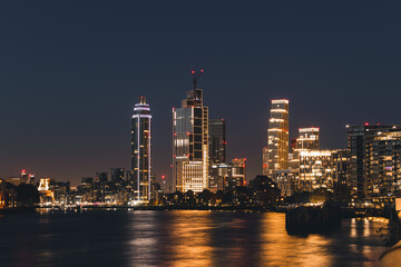 Fototapeta premium Illuminated skyscrapers in the London skyline at night reflecting on the Thames River
