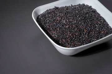 A bowl of black raw rice is placed on a dark table.The raw rice is spread out in the bowl, copy-space.