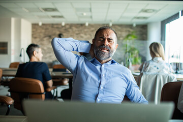Man experiencing neck pain while working on laptop in office