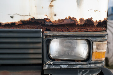 Close-up of a rusty truck front; corroded metal and peeling paint around the headlight and grille, symbolizing scrap metal recycling, body repair, and affordable auto parts.