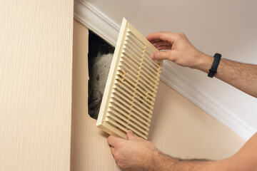 A man installs a plastic ventilation grid into a hole in a wall