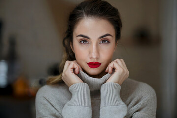 Retrato de mujer morena con labios rojos y jersey de cuello alto mirando a cámara. Generado con IA