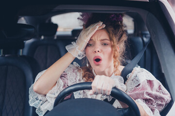 Historic elegance meets modern driving as a young woman in antique dress steers a car through urban...