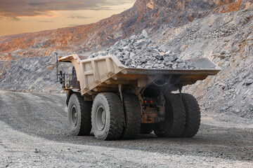 Massive Mining Dump Truck Transporting Rocks in Open-Pit Mine at Sunset