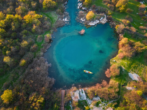 Aerial view of the serene Eye of Shegan karst spring surrounded by lush greenery and clear turquoise water, Bajze, Albania.