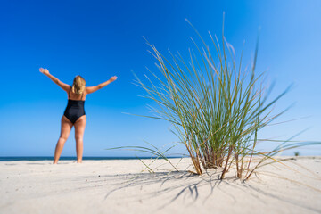 Middle aged woman in fashionable swimsuit  standing on sandy beach on summer day. 
Focus on...