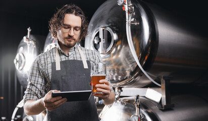 Brewer with clipboard examining control quality and color of drink production. Worker sommeliers...