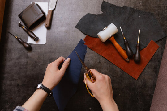 Concept small business footwear industry, shoemaker. Young woman tailor cutting brown leather patterns in atelier workshop