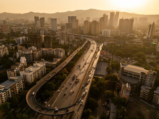Aerial view of a bustling cityscape with a modern bridge and heavy traffic under a beautiful sunset, Thane, India.