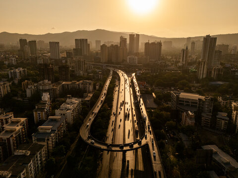 Aerial view of bustling traffic on a modern flyover with skyscrapers and beautiful sunset, Thane, India.