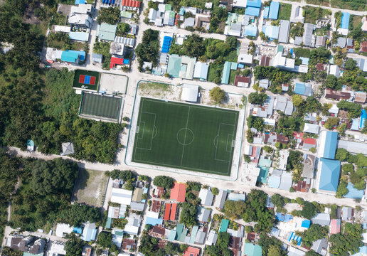 Aerial view of a lush local island with rooftops and a soccer field, Thoddoo, Maldives.