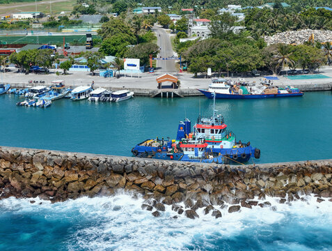 Aerial view of a scenic harbour with a dhoni boat moored at the pier amidst turquoise waves, Fuvahmulah, Maldives.