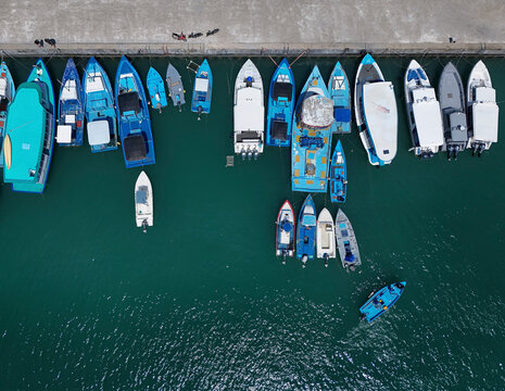 Aerial view of beautiful boats moored at a vibrant harbour with waves in the ocean, Fuvahmulah, Maldives.