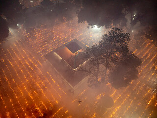 Aerial view of a mystical night festival with illuminated temple and gathering crowd surrounded by trees, Baradi, Bangladesh.