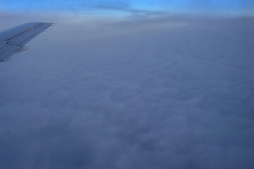 Fototapeta premium Thick layer of clouds under the wing of a flying airplane, winter vacation, airplane wing above the clouds.
