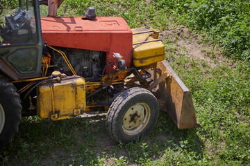 Obraz premium An old tractor clears a field of tall grass with a bucket, preparing the land for a construction project. A concept for building, engineering and transforming the countryside.