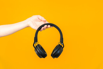Close up woman's hand holding large black wireless headphones. Isolated on a yellow background