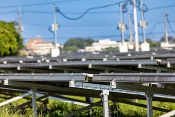 A row of solar panels in focus with a backdrop of urban infrastructure and power lines. 