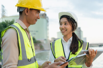 Two engineers in safety gear discuss project details using a tablet at an industrial refinery site...