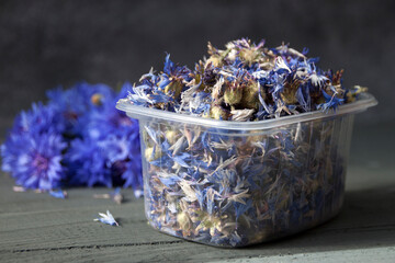 Dried cornflower flowers in open plastic container on wooden table