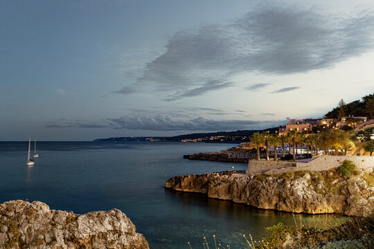 View of beautiful seaside village with sailboat near rocky coast at sunset, Castro, Italy.