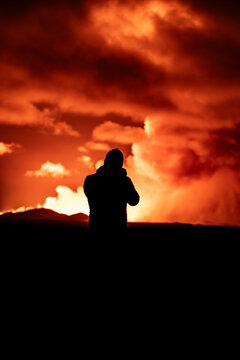 View of dramatic volcanic eruption with glowing lava and silhouetted figure against the night sky, Grindavik, Iceland.