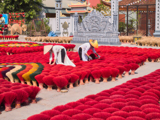 Workers arrange bright red incense sticks drying in a traditional Vietnamese village courtyard, ideal for: cultural travel stories, heritage features, spiritual themes and Asia tourism editorials.