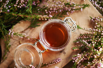A jar of herbal syrup with fresh wild heather flowers, top view