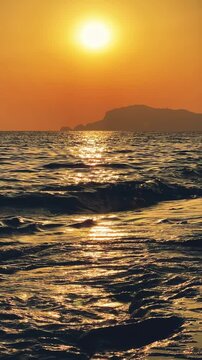 Sunset in Turkey, Alanya. The waves of the Mediterranean Sea roll over the sandy beach. The sunset is reflected in the water and slightly illuminates the city, against the background of Castle Hill.4К