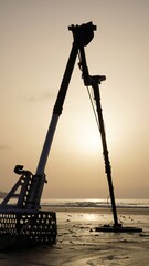 Silhouette of metal detector and shovel with holes on the shore. Working tools of a treasure hunter...