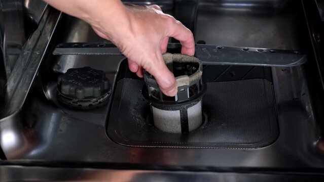 A hand taking out dishwasher filter to clean it, dis washer cleaning concept, kitchen home appliances care and maintenance