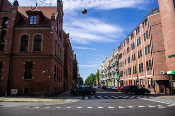 Obraz premium Street with red brick houses under a blue sky with a pedestrian crossing and parked cars.
