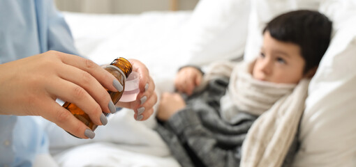 Mother pouring cough syrup for her ill little son in bedroom, closeup