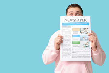 Shocked young man with newspaper on blue background