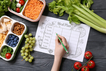 Woman making meal plan on dark wooden background